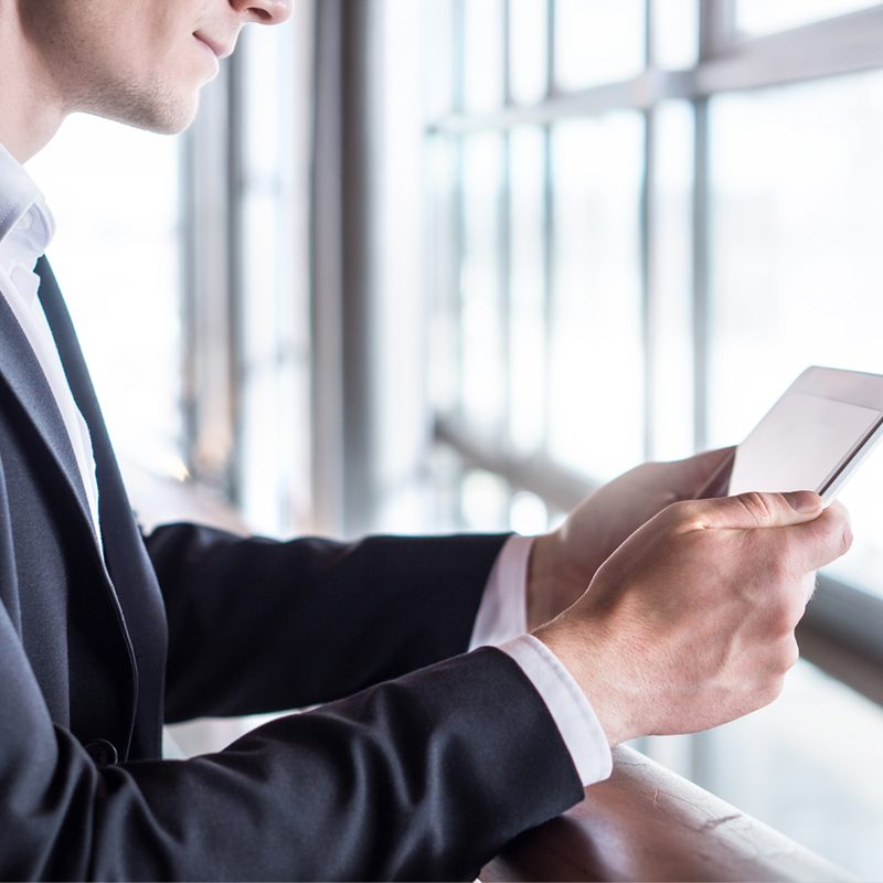 A commercial real estate broker reviewing deals on a smartphone by an office window.