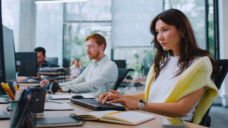 Two professionals working at their computers in an open-plan office.